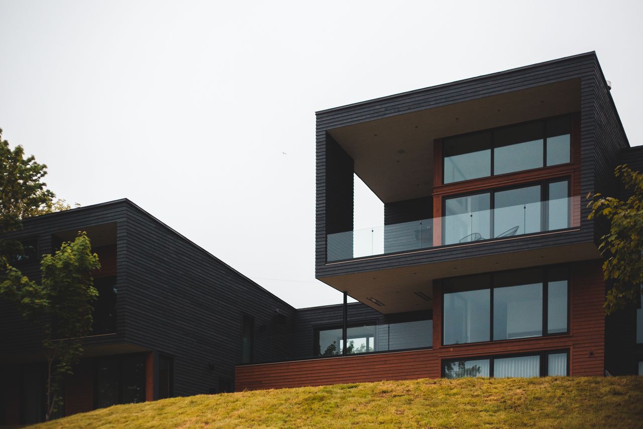 From below of contemporary geometric building with big windows and stylish design of balcony on green grass with trees